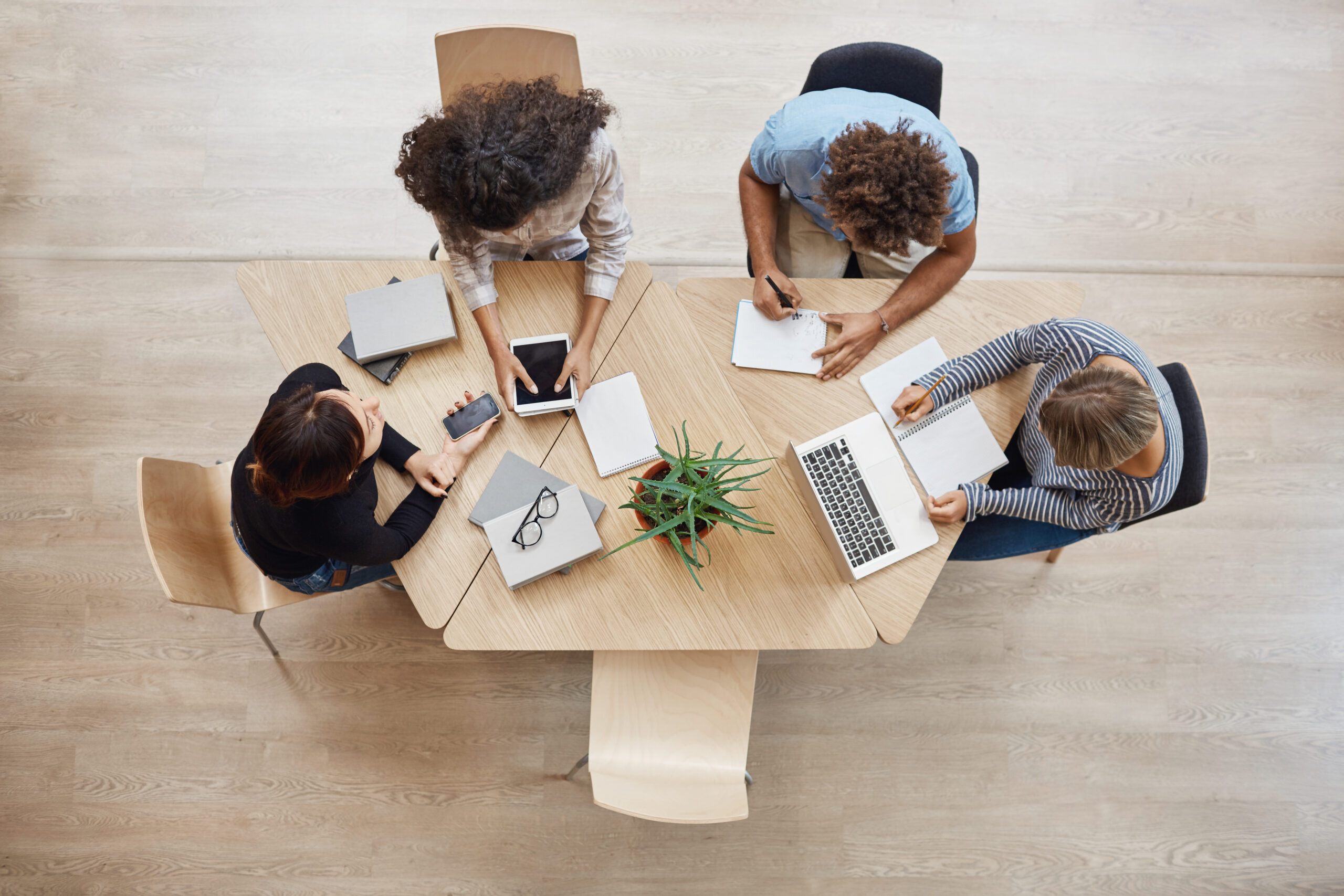 top view of 4 people having a meeting with notebooks, phones, laptops and tablets on the table